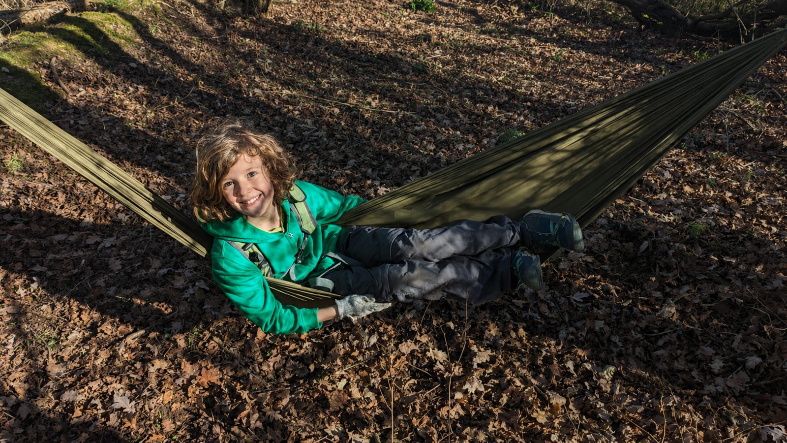 A smiling child relaxing in a green hammock among the autumn leaves