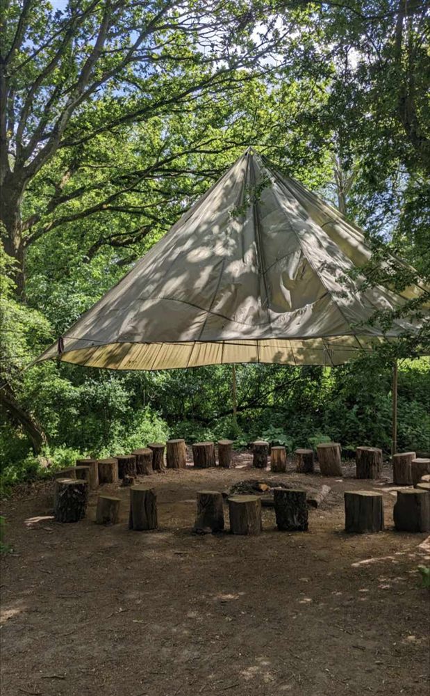 A tarpaulin shelter over a circle of log seats around the fire at our woodland site