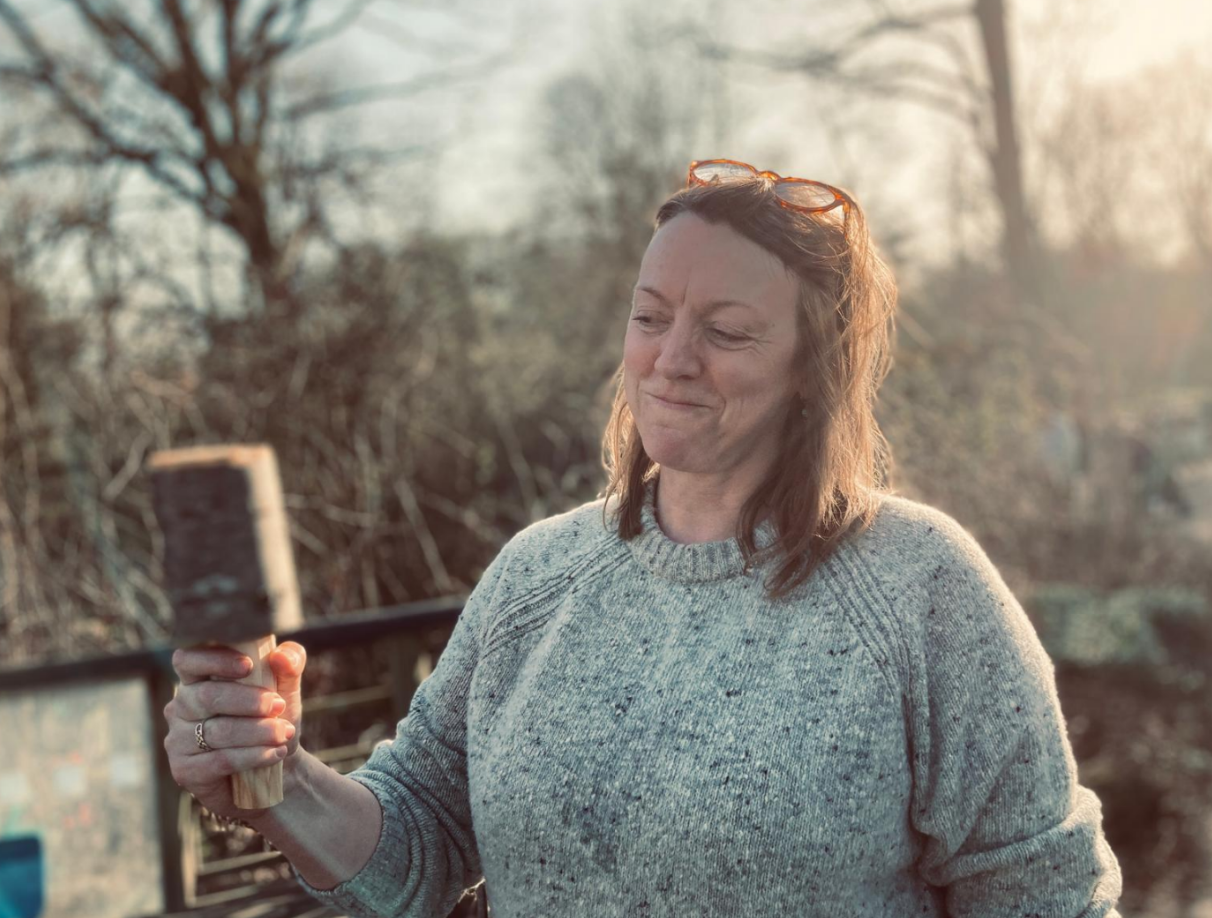 A trainee shaping a wooden mallet in golden afternoon light during the woodland training day