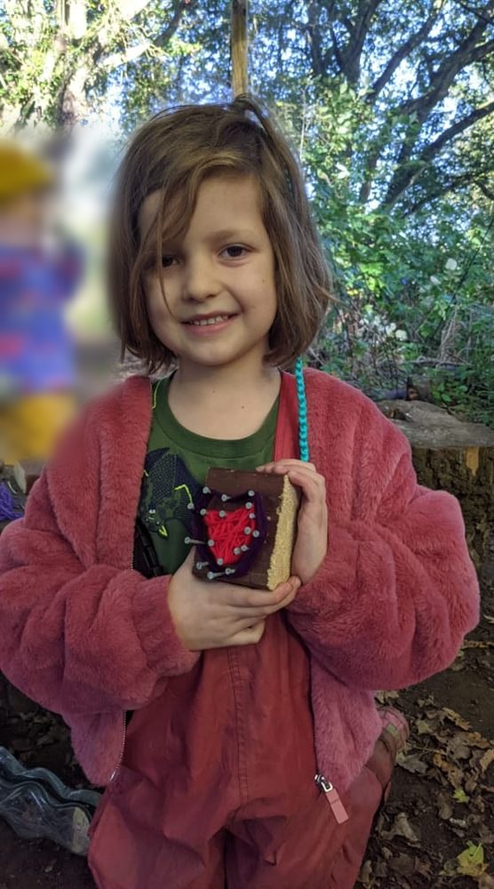 A child holding a woven heart craft made at Forest School